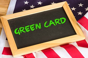 the words green card written on a small black chalkboard on top of a US flag