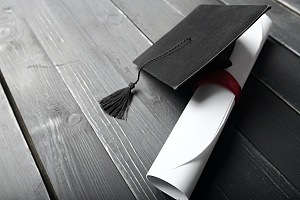 diploma and graduation cap on a black wooden floor