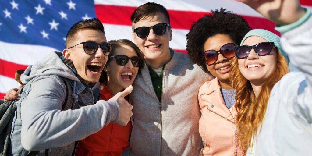 group of happy teenage friends taking selfie with smartphone and showing thumbs up over american flag background