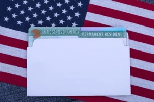 permanent resident card (Green card) in white envelope on American flag and blue fabric surface