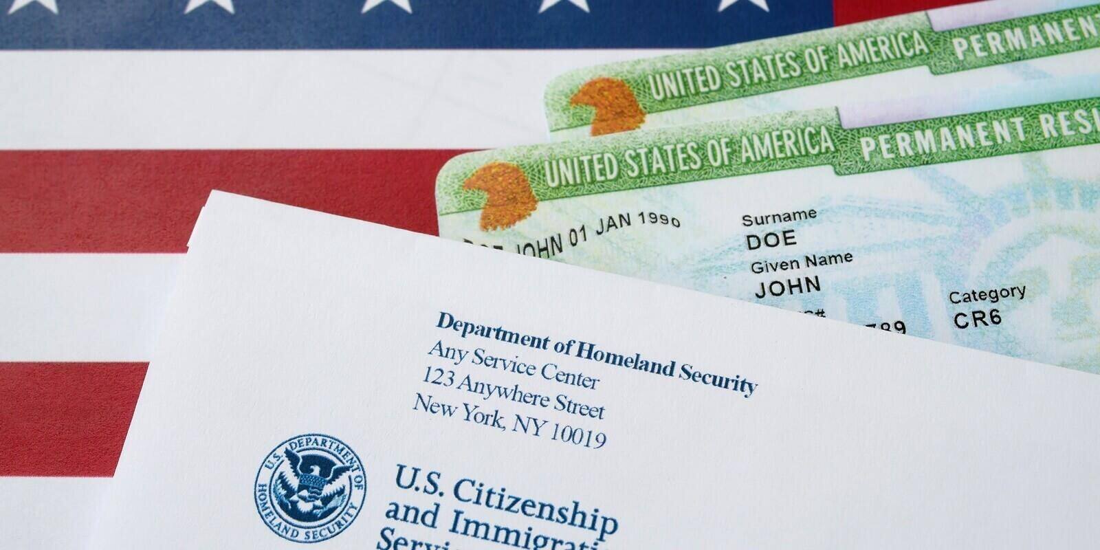 united states permanent resident green cards from dv-lottery lies on United States flag with envelope from department of homeland security
