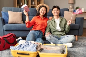 korean couple holding usa flag and tickets packing suitcase indoor